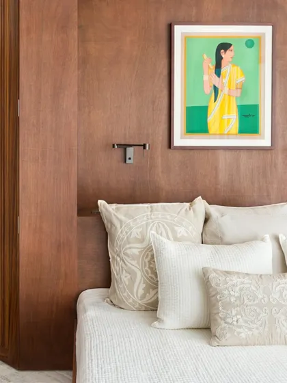 In the Limestone Residence, a wood-paneled wall creates a warm and intimate backdrop for the bed. The neutral-toned cushions and a piece of traditional Indian art complete the serene composition.