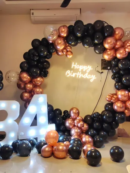 A stylish 34th birthday party with a black and rose gold theme, featuring a full circular balloon arch and large light-up marquee numbers.