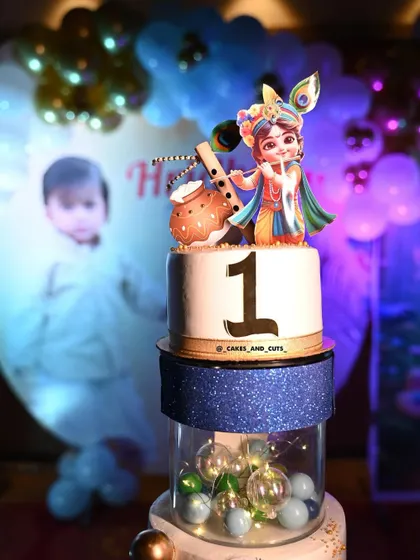 A close-up of the Krishna-themed cake, showing the beautiful details of the topper and the clear tier filled with lights.