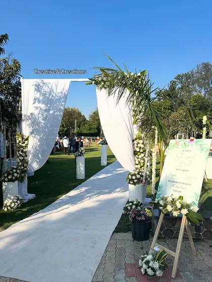 The entrance to a beautiful daytime wedding. The white floral arch and aisle are complemented by a welcome sign, setting a sophisticated tone for the event.