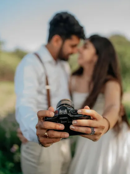 A creative shot focusing on the camera, with the couple blurred in the background. It’s a nod to the memories they are creating together.
