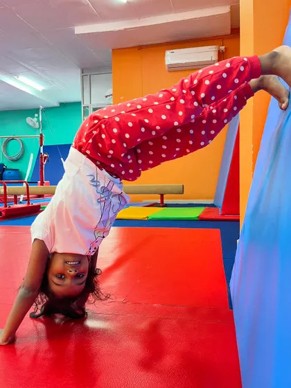An upside-down smile is the best kind of smile. This young gymnast is practicing a wall-assisted pose, building her strength and getting comfortable with being inverted.