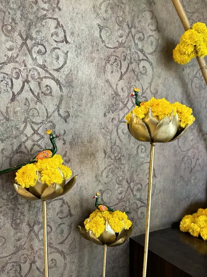 Delicate marigold blooms adorn golden lotus-shaped holders, each topped with a tiny peacock, a beautiful and intricate detail that honors Indian artistry.