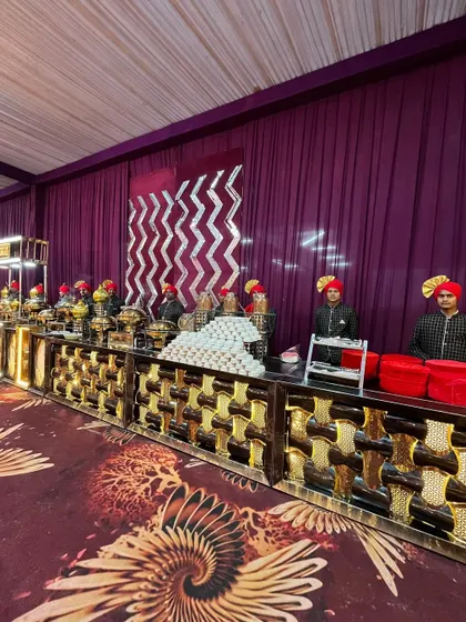 My staff, dressed in traditional attire with colorful turbans, stand ready behind a lavish buffet. The setup features a mix of modern illuminated counters and classic brassware, showing how I blend different styles for a unique look.