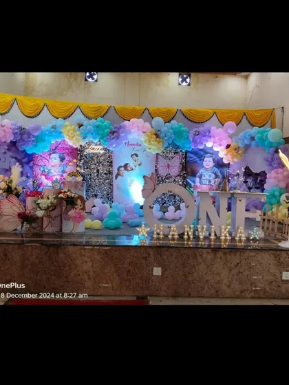 A grand butterfly-themed stage for Hanvika's first birthday. The setup uses pastel balloons, large butterfly props, and a sequin backdrop to create a dreamy effect.
