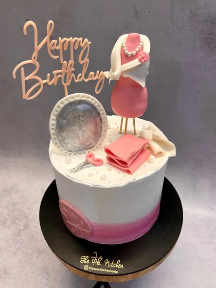 A fashion designer-themed cake, featuring a mannequin with a pink dress, a sewing kit, and a pin cushion, all handcrafted from fondant.