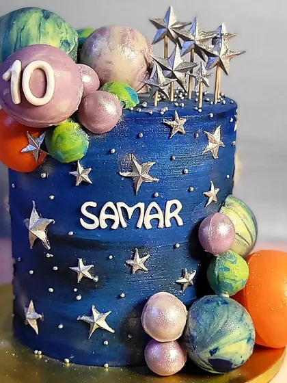 A galaxy-themed, all-buttercream cake for a 10th birthday. The deep blue cake is decorated with edible planets, stars, and a touch of sparkle.