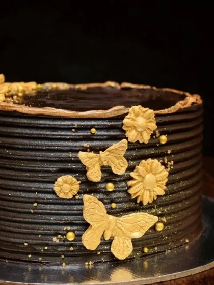 A minimalist take on a chocolate cake. This design features a textured dark chocolate ganache, decorated simply with delicate gold butterflies, flowers, and a sprinkle of gold dust.