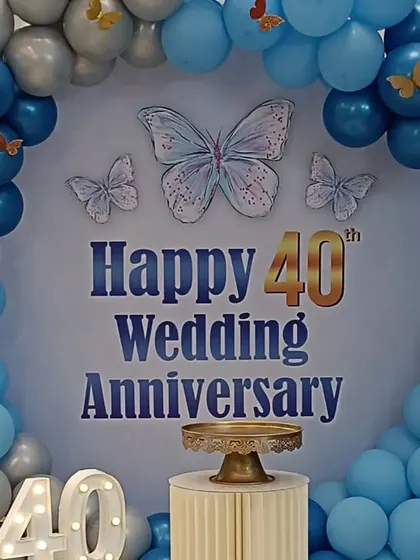 Celebrating a 40th wedding anniversary in style. This beautiful setup includes a circular backdrop, a blue and silver balloon arch with butterfly details, and light-up marquee numbers.