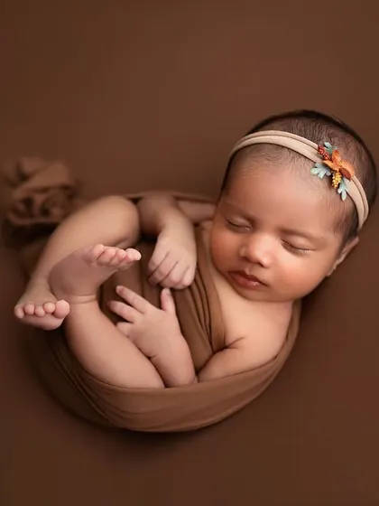 A beautiful "tucked-in" pose, where the baby is wrapped snugly with their little feet peeking out. The brown tones are warm and earthy.
