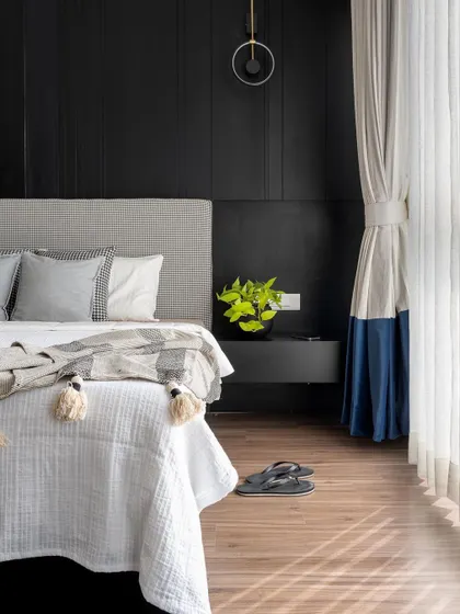 A detail shot of the bold black master bedroom. The contrast between the dark wall, the crisp white bedding, and the pop of blue in the color-blocked curtain adds a dynamic and stylish touch.
