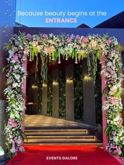 Beauty begins at the entrance. This stunning floral archway, overflowing with pink and white blooms and cascading greenery over a red carpet, creates an unforgettable first impression and welcomes guests into a world of celebration.