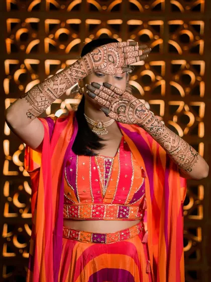 Rupa striking a classic bridal pose, her hands hiding her face, showcasing the intricate back-of-hand design.