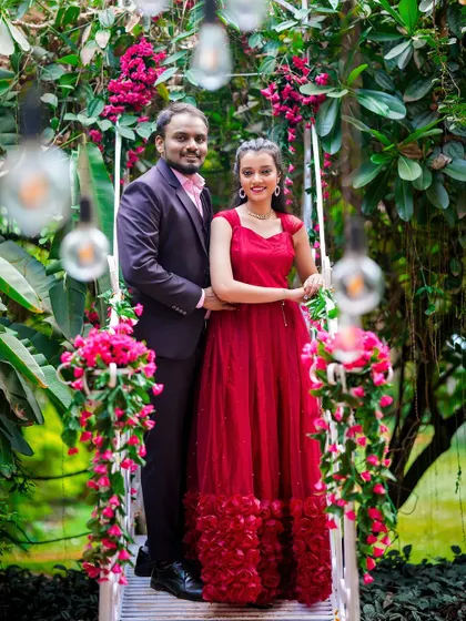 A fairytale-like pre-wedding photo of a couple on a floral swing, surrounded by hanging lights.
