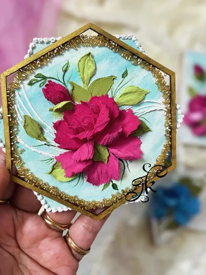 A hexagonal fridge magnet with a pink flower, framed with a sparkling gold border.