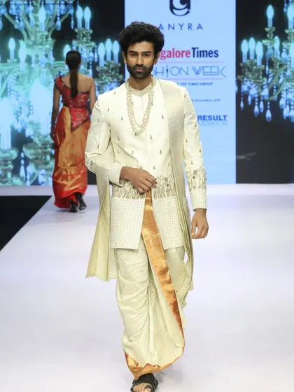 This runway look showcases a traditional South Indian outfit with a designer touch. The off-white and gold embroidered top is paired with a silk dhoti, demonstrating how heritage styles can be presented in a high-fashion context.