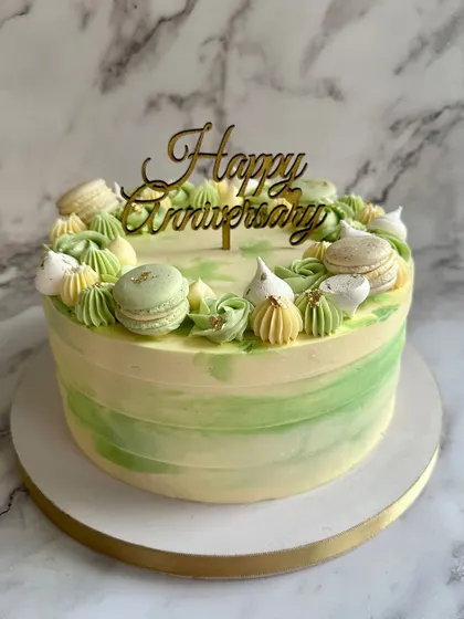 A fresh and vibrant anniversary cake in shades of green. The watercolor buttercream effect is beautifully complemented by piped details and delicate macarons.
