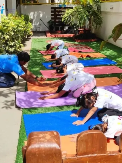 A teacher gently assists children with the child's pose in our outdoor garden. Practicing yoga in nature enhances the sense of calm and connection.