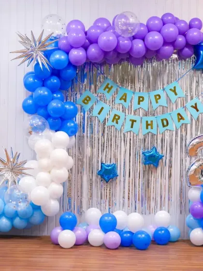 A blue and purple birthday setup with a silver foil curtain backdrop. This decoration includes a "Happy Birthday" banner, a balloon arch, and a number '2' foil balloon.