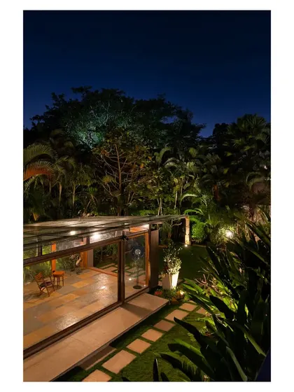 As dusk settles, the Komorebi Pavilion glows from within, highlighting the warm wooden structural elements. The surrounding garden is subtly lit, creating a serene and magical atmosphere that extends the usability of the space into the evening.
