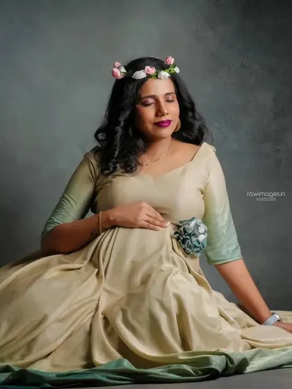 A peaceful portrait of the mother-to-be. The floral crown adds a delicate touch to the overall look, complementing the soft tones of the gown and the subtle makeup.