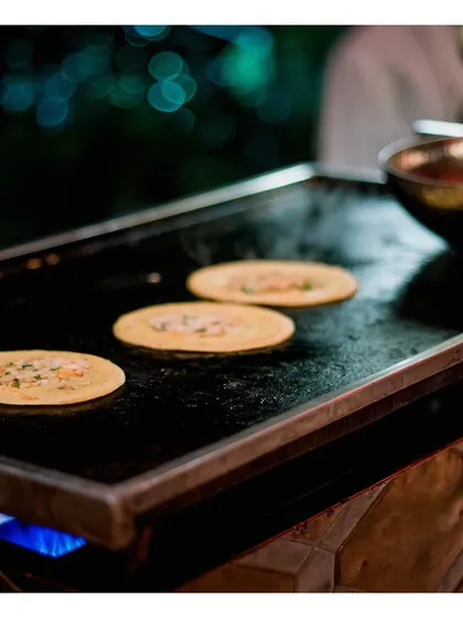 A live tawa station preparing mini uttapams, a popular South Indian delicacy. Guests love watching these savoury pancakes being made to order.