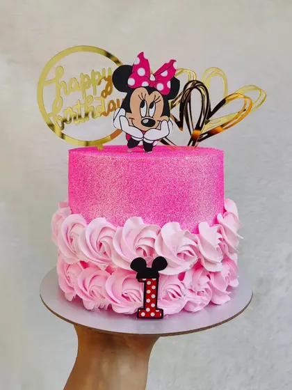 This glittering pink Minnie Mouse cake is perfect for a first birthday. The bottom tier is covered in buttercream rosettes, and the top sparkles with edible glitter.