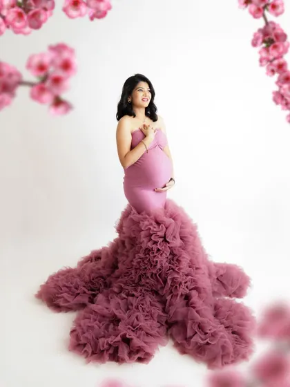 A joyful and vibrant portrait. The mom-to-be is surrounded by pink blossoms, her ruffled mauve gown creating a stunning visual.