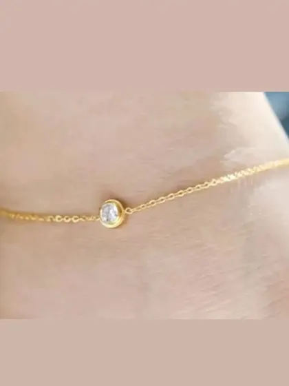 A delicate gold-toned anklet featuring a single, sparkling bezel-set crystal. It's a simple and elegant accessory for any occasion.