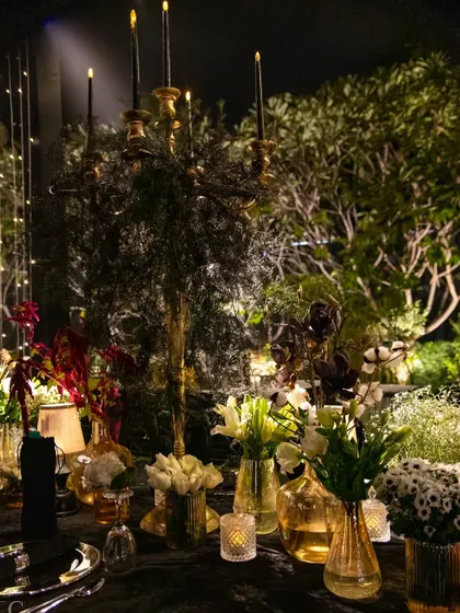 A grand candelabra with black taper candles rises from a bed of foliage, creating a dramatic and gothic-inspired centerpiece. This piece is perfect for a moody and atmospheric event.