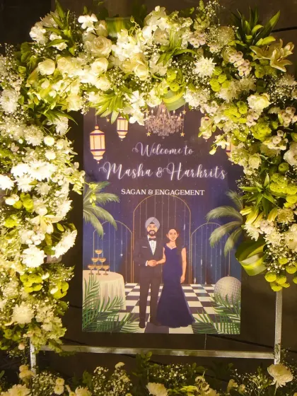 A custom illustrated welcome sign for Masha and Harkrit's Sagan and Engagement, framed by a beautiful arch of fresh white and green florals.