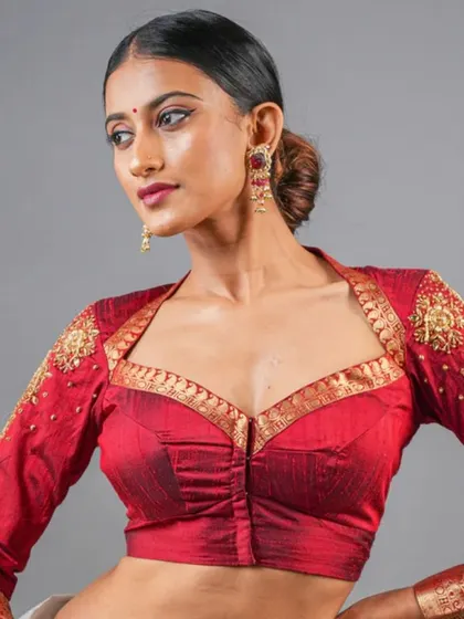 This striking red blouse features a unique neckline and heavy Zardosi embroidery on the sleeves, making it a bold and beautiful choice for a bride or wedding guest.