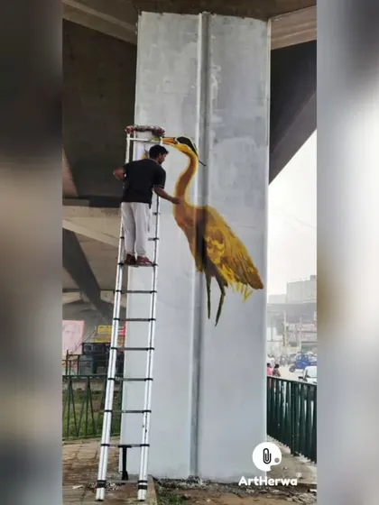 An artist at work on a tall ladder, painting a beautiful heron on a pillar in Chandigarh.