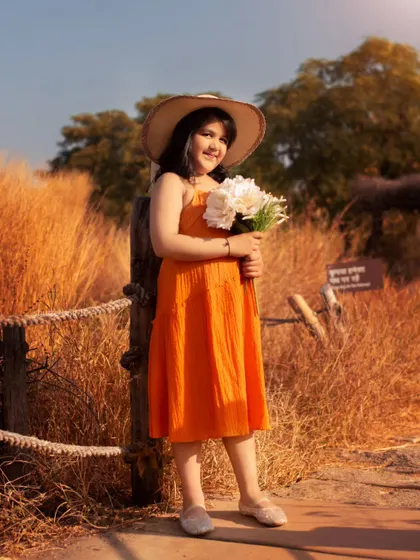 This young lady looks so chic in her orange dress and sunhat, holding a bouquet of flowers in a field of tall grass.
