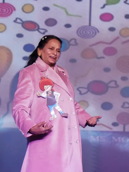 A senior citizen participant shines on stage in a pink coat during a special performance segment.