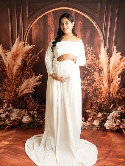 A serene portrait in a classic white off-the-shoulder gown. The warm, rustic backdrop adds a touch of earthy elegance.