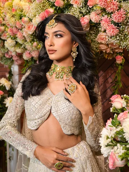 The floral background adds a touch of romance to this sophisticated white lehenga look, highlighting the bride's radiant makeup.