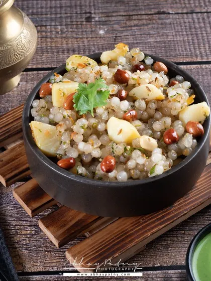 Sabudana Khichdi, a popular fasting meal, is presented here in a rustic bowl. The dark wooden textures complement the earthy tones of the dish.