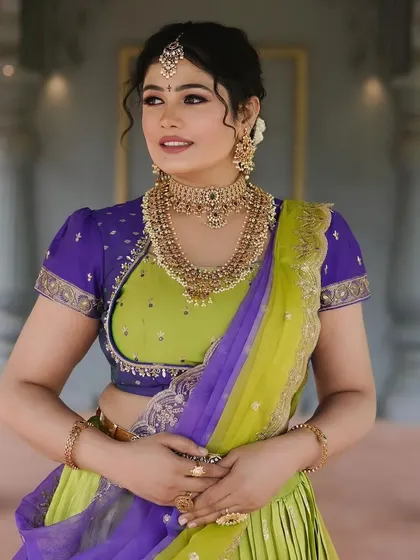 A model looking graceful in a lime green and purple half-saree, paired with a traditional gold-finish choker and haram set.