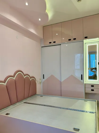 A beautiful bedroom for a princess. The design includes a custom scalloped headboard, pink and white sliding wardrobes, and a matching dressing table with a lit mirror.