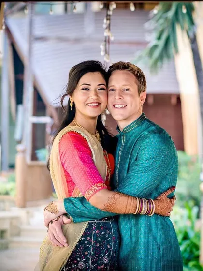 A happy, classic portrait of the couple. Their bright smiles and warm embrace showcase their love and the colorful joy of their Indian wedding celebration.
