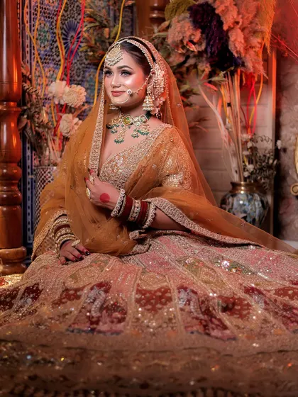 A regal, seated portrait of the bride. Her voluminous lehenga spreads around her, and the rich, warm lighting of the decorated room creates an opulent and luxurious atmosphere.