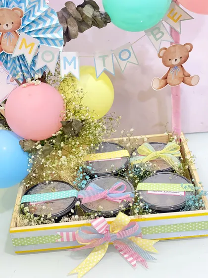 A detailed shot of the Yauatcha food hamper for the mom-to-be. You can see the individual food containers tied with beautiful ribbons, nestled among flowers and "Mom to Be" decorations.
