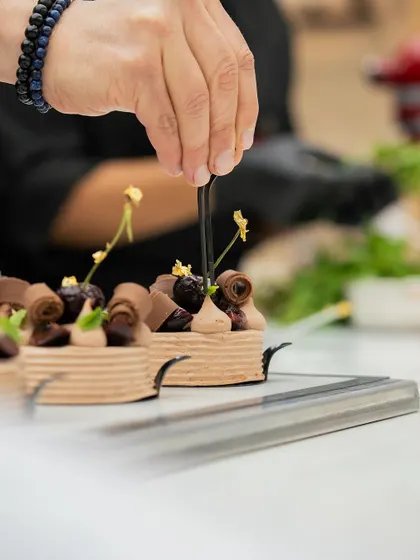 A chef adds the final decorative touches to a series of intricate chocolate tarts.