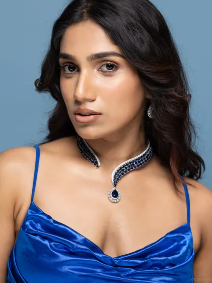 A model wearing an elegant sapphire and diamond necklace set against a royal blue dress. The styling complements the jewellery, making it the hero of the shot.