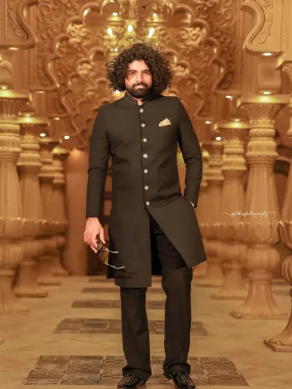 A formal and dramatic series of a model in a black sherwani. The shots are taken in unique studio settings, one with dramatic blue spotlights and another with a wall of chandeliers, creating a high-end, luxurious feel.