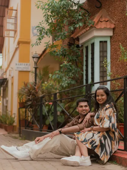 A relaxed portrait of a couple sitting together in the charming, colorful streets of Goa, showcasing the unique architecture and vibrant atmosphere of the location.