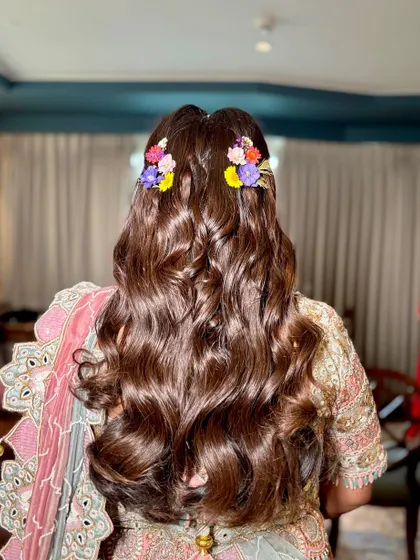 A beautiful half-up hairstyle with voluminous curls, decorated with colorful fresh flowers for a daytime event.