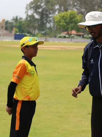 A coach gives instructions to two young captains on the pitch before the start of their match.