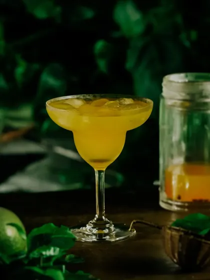 A shot of the finished passion fruit cocktail in a glass, set against a lush green background.